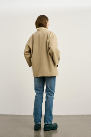 Beige jakke med løs pasform og lange ærmer, parret med blå jeans og grønne sko. Designet af MEOTINE.