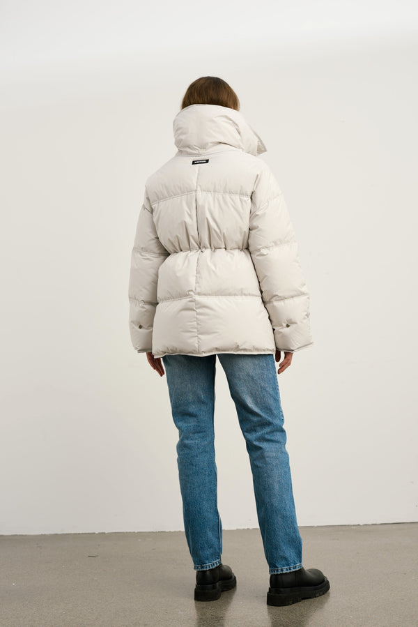 Lys beige MEOTINE jakke med høj krave, bæres af en person set bagfra, kombineret med blå jeans og sorte støvler.