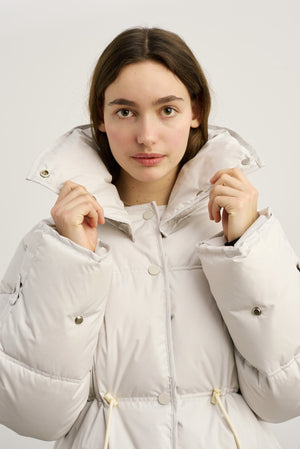 Lys, pufferjakke fra MEOTINE med høj krave, præsenteret af en ung kvinde, der holder kraven op.