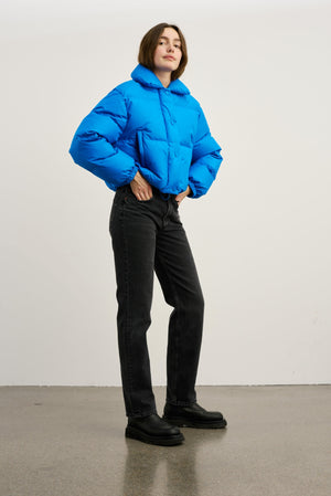 Blå, kort pufferjakke med hætte og elastiske manchetter, parret med sorte jeans og støvler. MEOTINE-stil til hverdag.