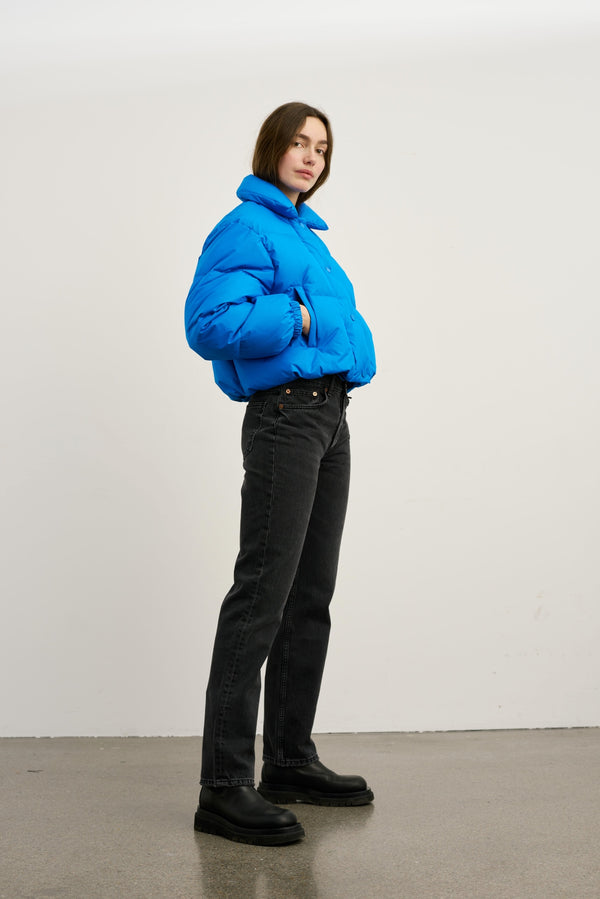 Blå, quilted jakke fra MEOTINE, stylet med sorte jeans og støvler, præsenteret i en minimalistisk indendørs setting.