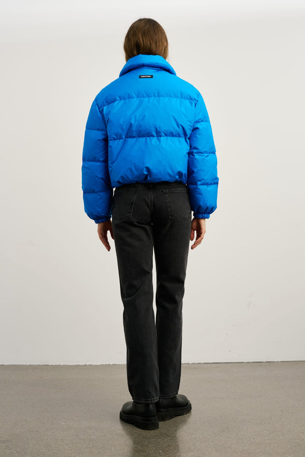 Blå pufferjakke fra MEOTINE, set bagfra, kombineret med sorte bukser og støvler, på en neutral baggrund.