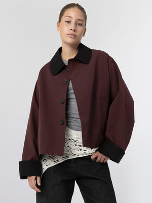 Oversized bordeaux jakke med sort krave og knapper, stylet med en grå top og hvid bluse, fra MEOTINE.