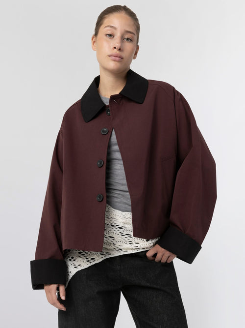 Oversized bordeaux jakke med sort krave og knapper, stylet med en grå top og hvid bluse, fra MEOTINE.