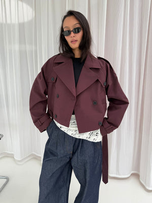 Stilfuld bordeaux trenchcoat fra MEOTINE, båret af en model med solbriller, kombineret med en hvid bluse og denimbukser.