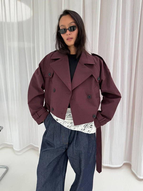 Stilfuld bordeaux trenchcoat fra MEOTINE, båret af en model med solbriller, kombineret med en hvid bluse og denimbukser.