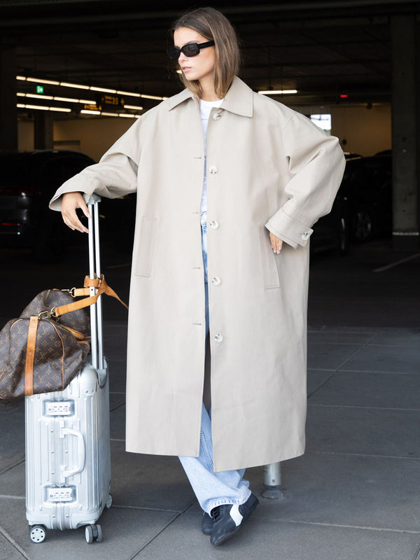 Lang beige frakke fra MEOTINE, perfekt til en stilfuld rejse med kuffert i hånden.