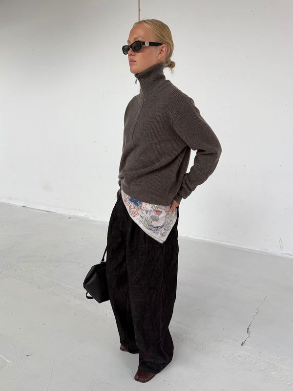 Modellen bærer en grå striktrøje med høj hals og sorte bukser, kompletteret med solbriller og en taske fra MEOTINE.