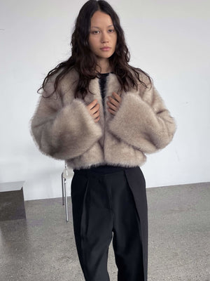 Lys beige faux fur jakke fra MEOTINE, med brede ærmer og en kort pasform, båret af en model i en minimalistisk indretning.