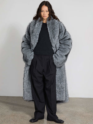 Luksuriøs grå pelsfrakke fra MEOTINE, båret over en sort trøje og sorte bukser, med en moderne og stilfuld silhuet.