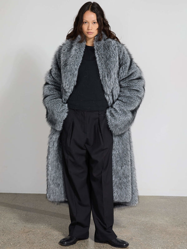 Luksuriøs grå pelsfrakke fra MEOTINE, båret over en sort trøje og sorte bukser, med en moderne og stilfuld silhuet.