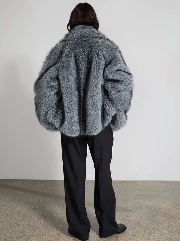 Grå, fluffy jakke fra MEOTINE set bagfra, kombineret med sorte bukser, der skaber et elegant og moderne look.