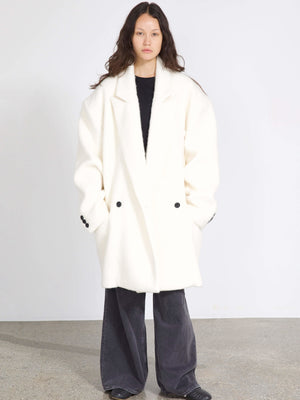 Oversized hvid frakke med sorte knapper, båret af model med langt hår, perfekt til en stilfuld MEOTINE-look.