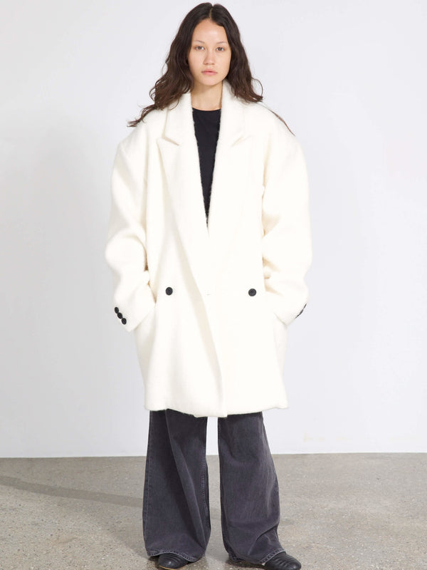 Oversized hvid frakke med sorte knapper, båret af model med langt hår, perfekt til en stilfuld MEOTINE-look.