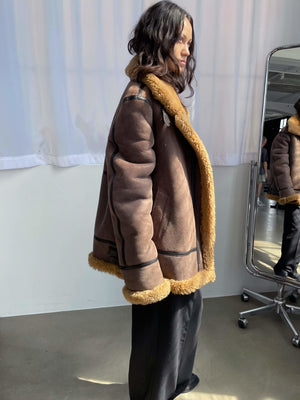 Brun jakke med faux fur-finish og detaljer i sort, fra MEOTINE, set fra siden i et lyst rum med spejl.