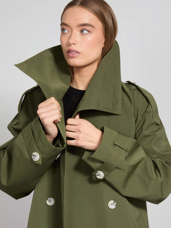 Grøn MEOTINE trenchcoat med store knapper og høj krave, båret af en model med naturlig makeup og let bølget hår.