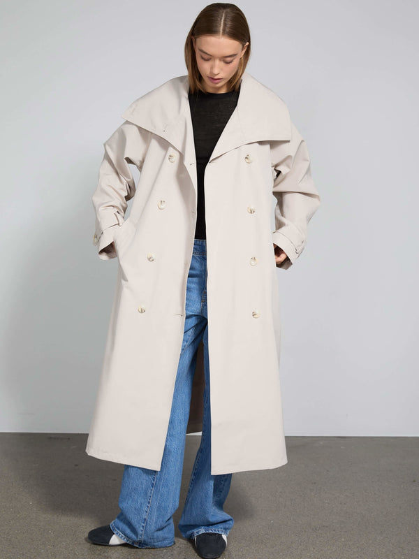 Lang beige trenchcoat med store knapper og bred krave, båret af en model med afslappet stil. MEOTINE tilføjer elegance til looket.