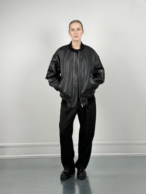 Sort læderjakke med afslappet pasform, kombineret med sorte bukser, fra MEOTINE, præsenteret på en model i et minimalistisk rum.