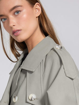 Elegant kvinde iført en grå MEOTINE trenchcoat, der fremhæver hendes ansigt og naturlige skønhed.