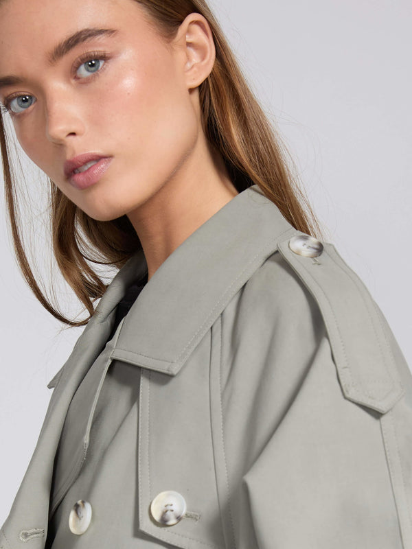 Elegant kvinde iført en grå MEOTINE trenchcoat, der fremhæver hendes ansigt og naturlige skønhed.