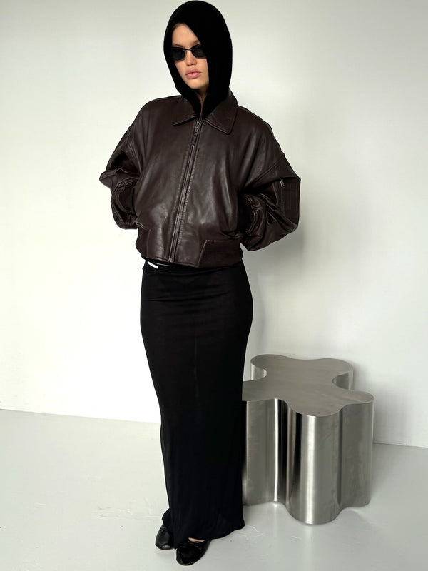 Model in a brown bomber jacket and black skirt, wearing sunglasses and a hood, showcasing MEOTINE's stylish look.