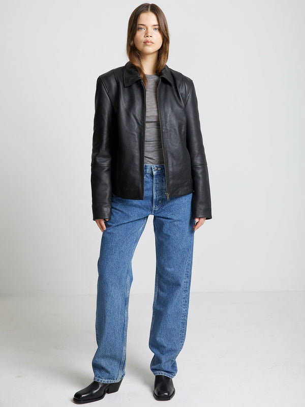 Sort læderjakke fra MEOTINE, parret med grå top og blå jeans, præsenteret af en model i et lyst rum.