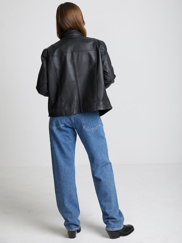 Sort læderjakke fra MEOTINE, set bagfra, kombineret med blå jeans og sorte støvler, på en neutral baggrund.