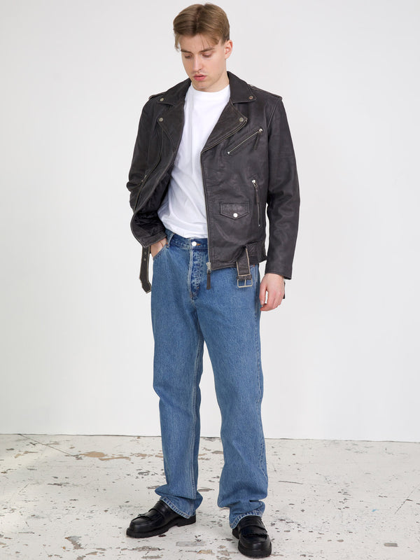 Mand iført en sort læderjakke og blå jeans, står på en lys baggrund. Jakken er fra MEOTINE.