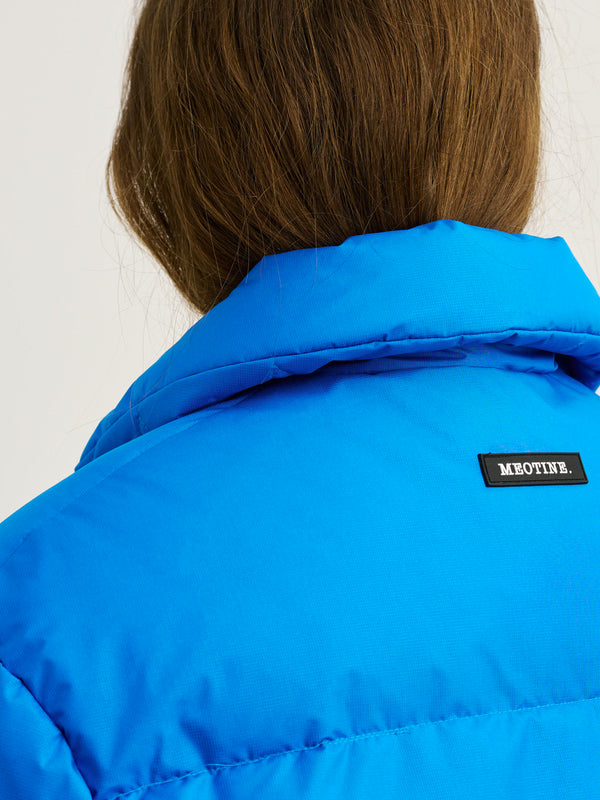 Blå jakke med høj krave og MEOTINE-logo, set fra ryggen, fremhæver en moderne og stilfuld look.