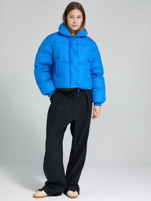 Blå, cropped jakke fra MEOTINE med knaplukning og hætte, parret med sorte, løse bukser for et moderne look.