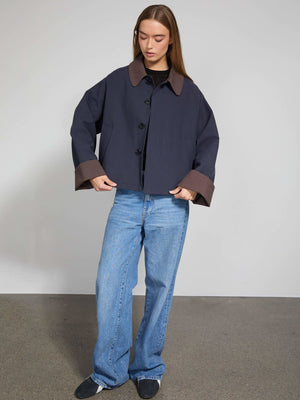 Stilfuld jakke fra MEOTINE i navy med brune detaljer, parret med løse jeans og en sort top, præsenteret i et minimalistisk rum.