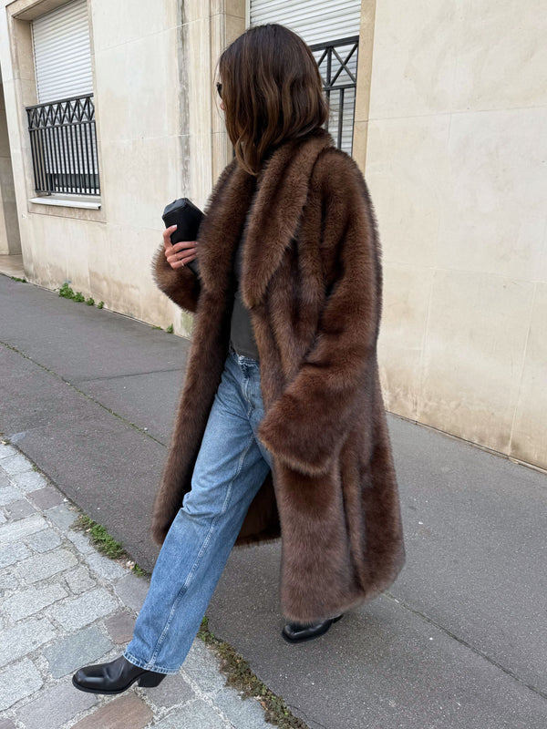 Elegant kvinde iført en MEOTINE pelsfrakke og jeans, der går langs en gade med en afslappet stil.