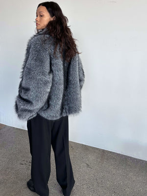 Grå pelsjakke fra MEOTINE, bæredygtig og stilfuld, bæres med sorte bukser og en moderne silhuet.