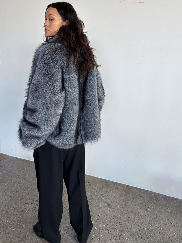 Grå pelsjakke fra MEOTINE, bæredygtig og stilfuld, bæres med sorte bukser og en moderne silhuet.
