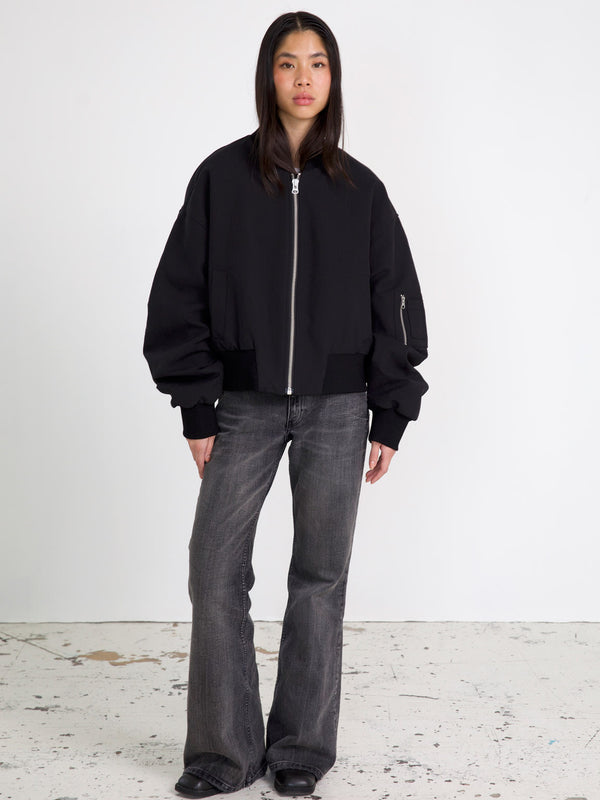 Sort bomberjakke med bredde og lynlås, parret med grå flared jeans. MEOTINE tilføjer et moderne touch til din garderobe.