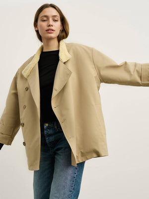 Beige jakke med pelskrave, iført af en model med sort t-shirt og jeans. MEOTINE tilføjer stil og komfort til din garderobe.