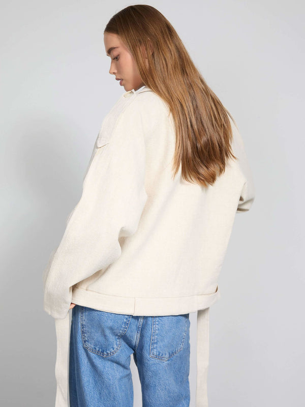 Lys beige jakke fra MEOTINE med løs pasform, lange ærmer og bånddetaljer, set bagfra på en model med langt hår.
